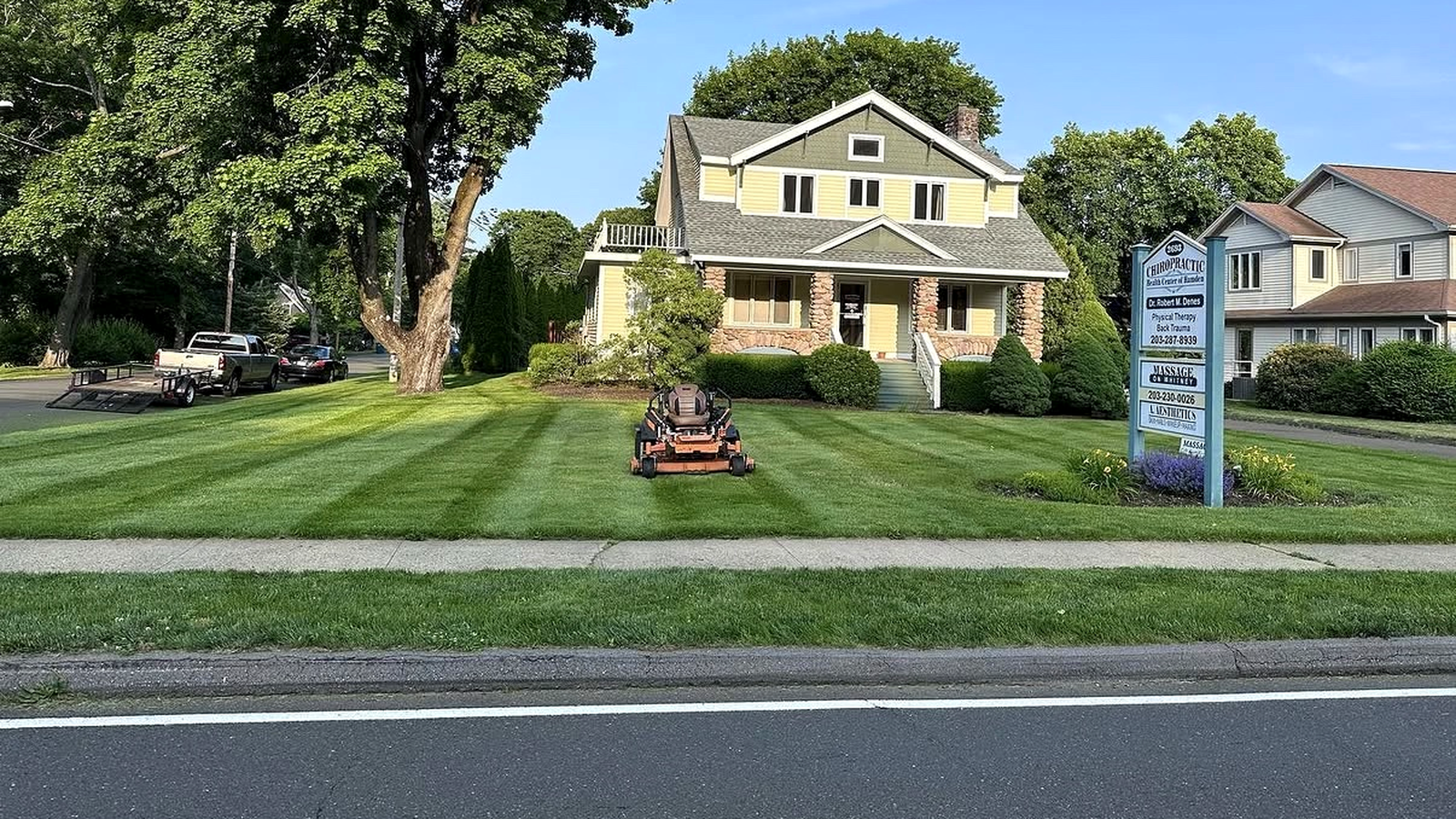 Premier Property Maintenance crew mowing a striped lawn in front of a New England home